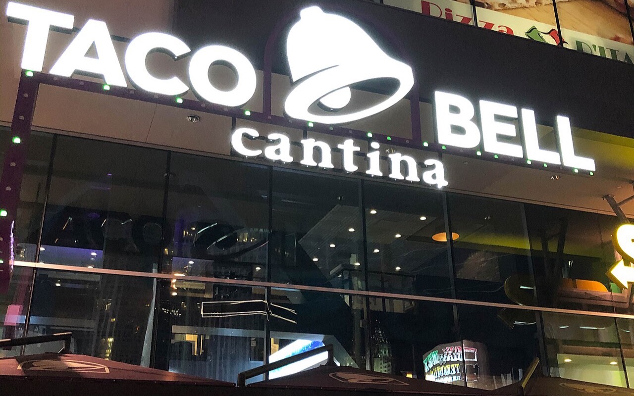 The Taco Bell Cantina sign above the restaurant's glass frontage at Harmon Corner on the Strip at night